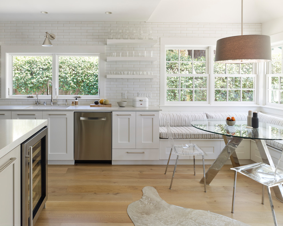 Example of a transitional light wood floor and beige floor kitchen design in San Francisco with an undermount sink, shaker cabinets, white cabinets, white backsplash, subway tile backsplash, stainless steel appliances, an island and gray countertops