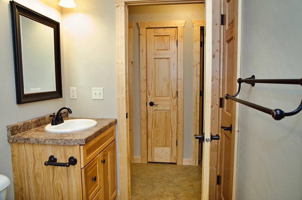 Mid-sized country master bathroom in Other with recessed-panel cabinets, light wood cabinets, a drop-in tub, a shower/bathtub combo, a two-piece toilet, beige tile, beige walls, linoleum floors, a drop-in sink, laminate benchtops, brown floor and a shower curtain.