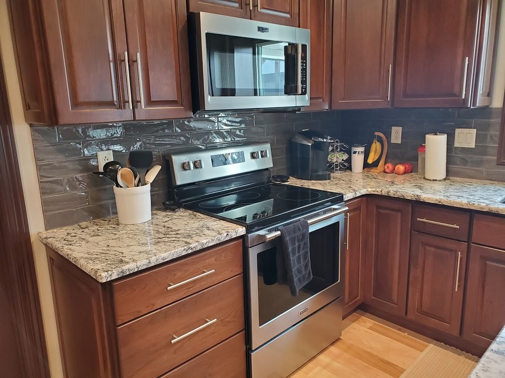 Example of a large transitional u-shaped light wood floor and multicolored floor eat-in kitchen design in Cedar Rapids with an undermount sink, raised-panel cabinets, dark wood cabinets, granite countertops, metallic backsplash, ceramic backsplash, stainless steel appliances, an island and gray countertops