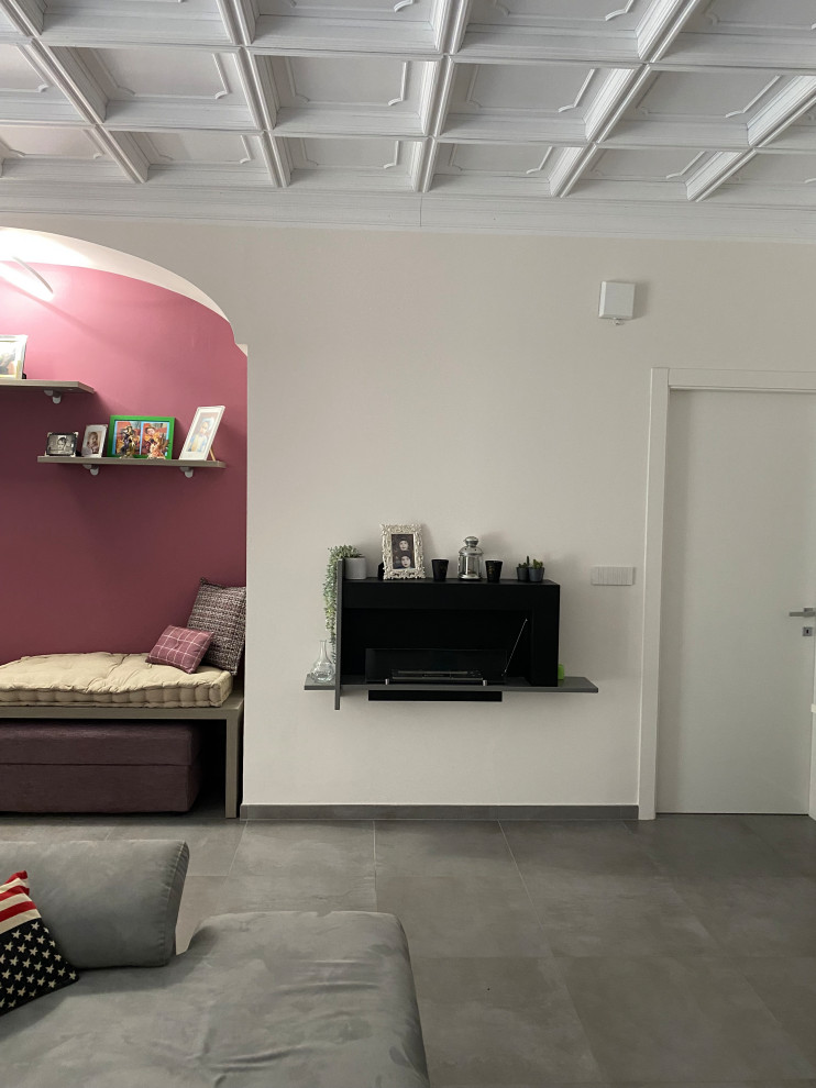 Imagen de sala de estar abierta moderna pequeña con paredes blancas, suelo de baldosas de porcelana, chimeneas suspendidas, marco de chimenea de metal, pared multimedia, suelo gris y casetón