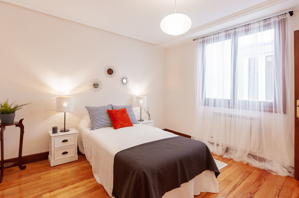 Modelo de dormitorio principal tradicional renovado con paredes blancas y suelo de madera en tonos medios