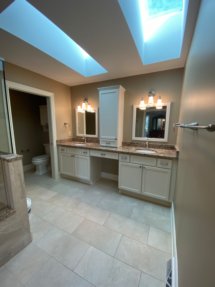 Inspiration for a large traditional master bathroom in Cleveland with recessed-panel cabinets, white cabinets, a corner shower, a two-piece toilet, beige tile, porcelain tile, beige walls, porcelain floors, an undermount sink, granite benchtops, beige floor, a hinged shower door, brown benchtops, an enclosed toilet, a double vanity and a built-in vanity.