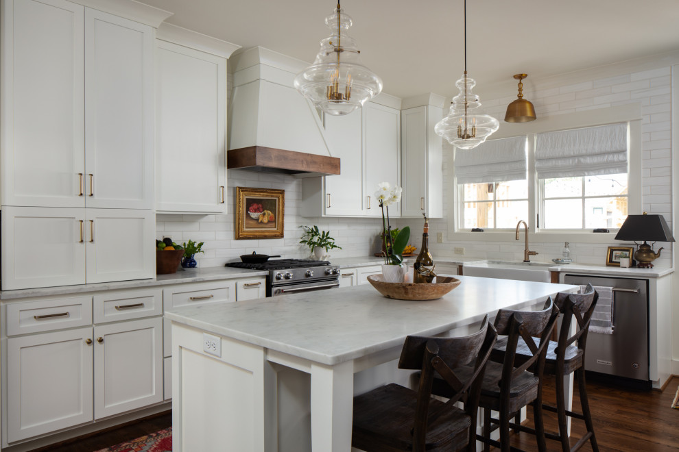 This is an example of a mid-sized traditional l-shaped open plan kitchen in Birmingham with a farmhouse sink, recessed-panel cabinets, white cabinets, marble benchtops, white splashback, ceramic splashback, stainless steel appliances, dark hardwood floors, with island, brown floor and grey benchtop.