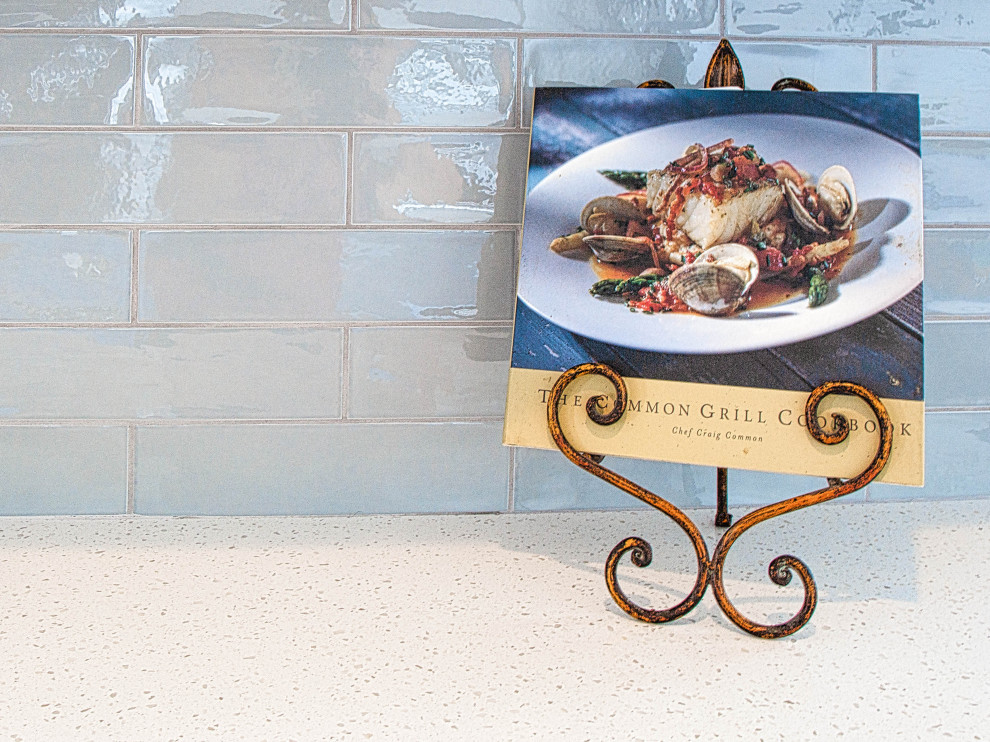Cette photo montre une grande cuisine américaine linéaire bord de mer avec un placard à porte shaker, des portes de placard blanches, un plan de travail en quartz modifié, une crédence bleue, une crédence en carreau de porcelaine, îlot et un plan de travail blanc.