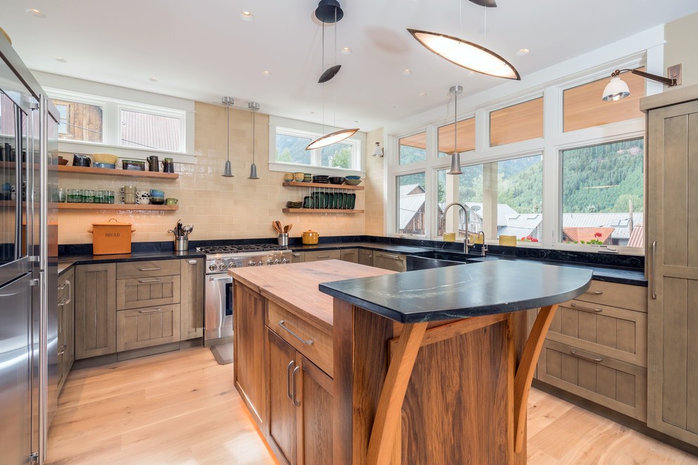 Inspiration for a mid-sized rustic u-shaped light wood floor and beige floor enclosed kitchen remodel in Denver with a farmhouse sink, shaker cabinets, medium tone wood cabinets, soapstone countertops, beige backsplash, subway tile backsplash, stainless steel appliances and an island