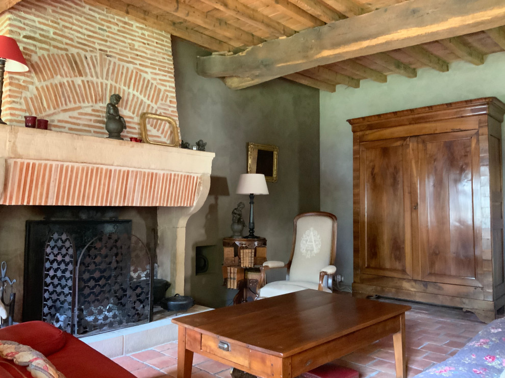 This is an example of a mid-sized country open concept living room in Grenoble with beige walls, terra-cotta floors, a standard fireplace, a brick fireplace surround, no tv, orange floor and exposed beam.