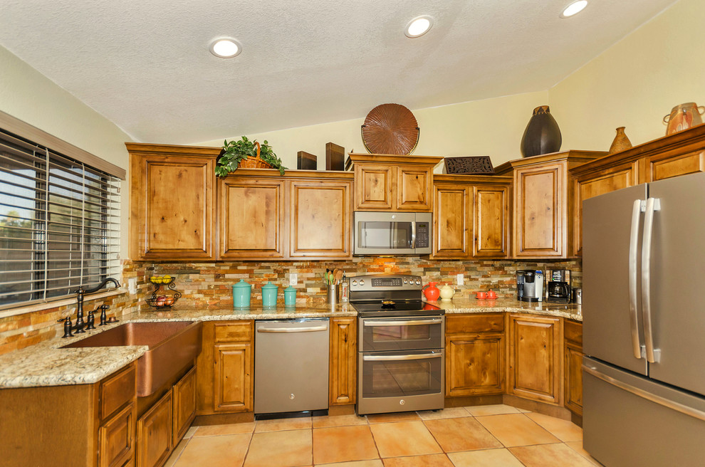 Home design - mid-sized rustic u-shaped porcelain tile home design idea in Phoenix with a farmhouse sink, raised-panel cabinets, medium tone wood cabinets, granite countertops, orange backsplash, stone tile backsplash, stainless steel appliances and no island
