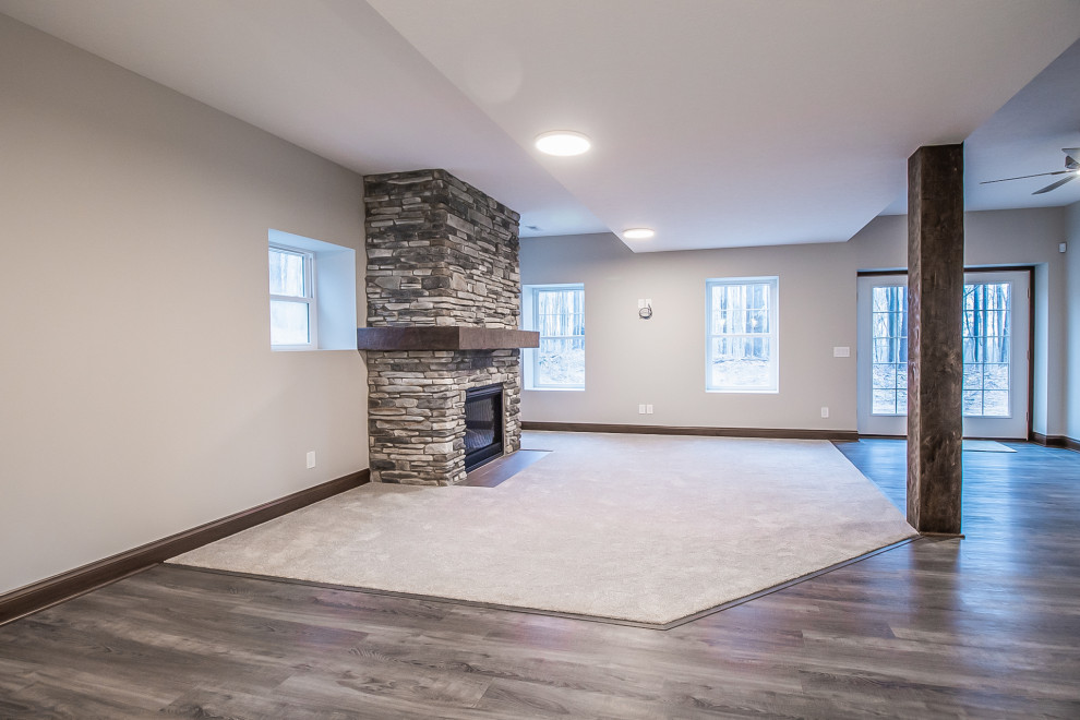 Photo of a large classic walk-out basement in Cleveland with grey walls, carpet, a standard fireplace, a stacked stone fireplace surround and grey floors.