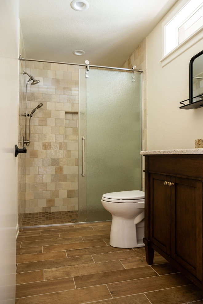 This is an example of a mid-sized 3/4 bathroom in Other with shaker cabinets, dark wood cabinets, an alcove shower, a one-piece toilet, beige tile, ceramic tile, white walls, wood-look tile, an undermount sink, granite benchtops, brown floor, a sliding shower screen, beige benchtops, a niche, a single vanity and a freestanding vanity.