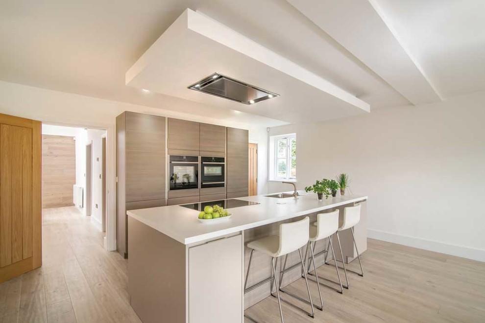 Inspiration for a contemporary kitchen in Cheshire with a single-bowl sink, flat-panel cabinets, medium wood cabinets, black appliances, light hardwood floors and with island.
