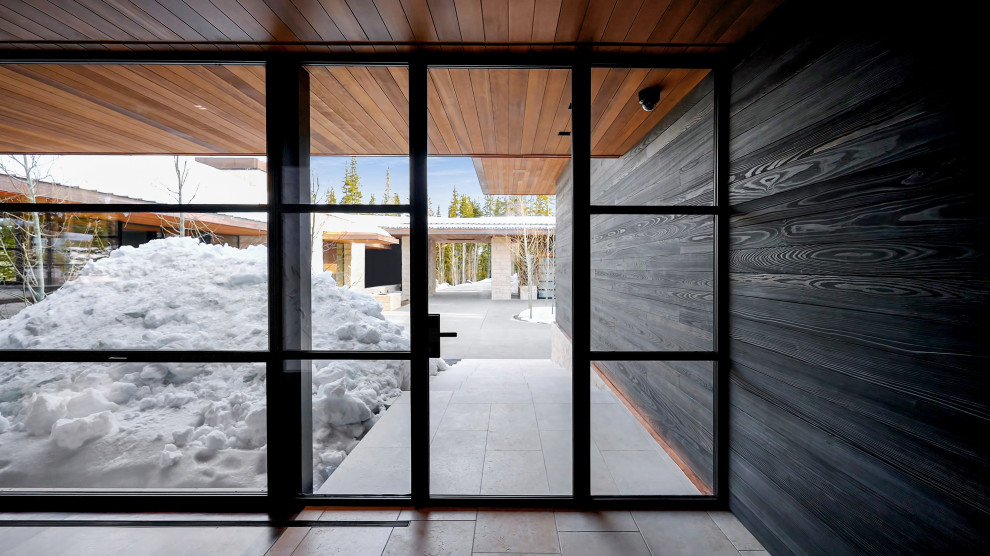 Cette photo montre une entrée moderne en bois de taille moyenne avec un mur noir, un sol en calcaire, une porte simple, une porte en verre, un sol beige et un plafond en bois.