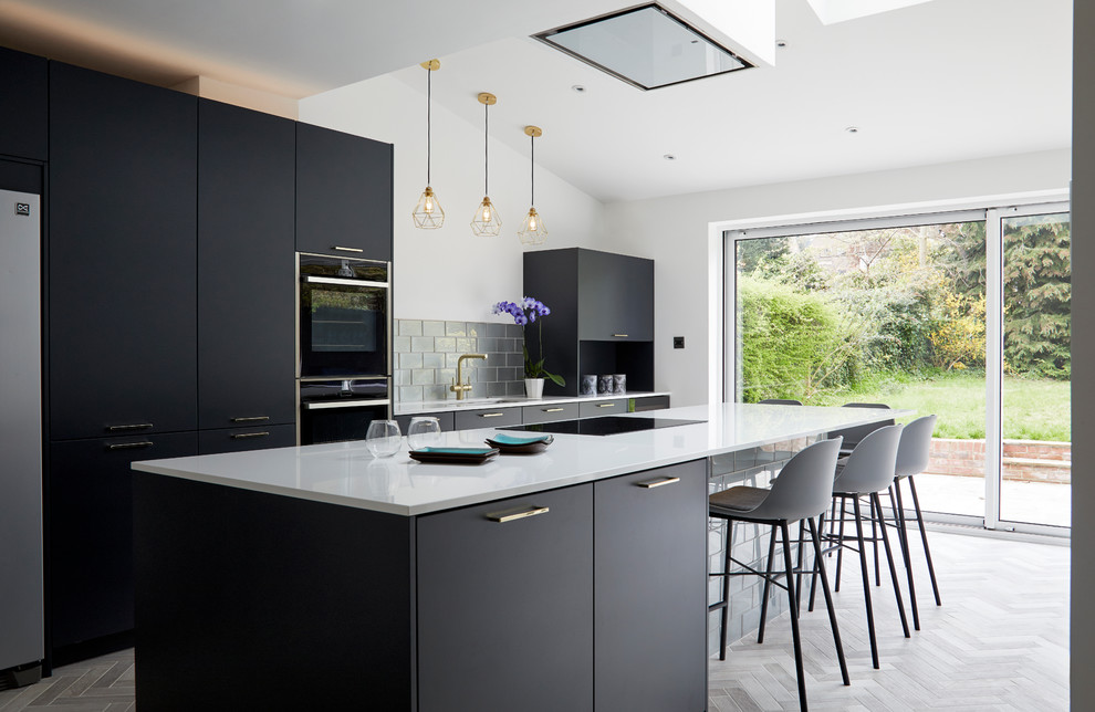 Inspiration for a large contemporary open plan kitchen in Kent with a drop-in sink, flat-panel cabinets, blue cabinets, solid surface benchtops, metallic splashback, glass tile splashback, black appliances, porcelain floors, with island, grey floor and white benchtop.