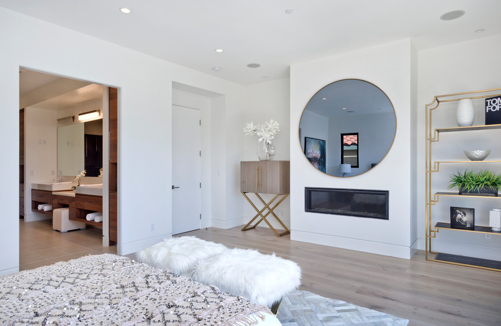 Photo of a mid-sized contemporary master bedroom in Orange County with white walls, light hardwood floors, a ribbon fireplace, a metal fireplace surround and beige floor.