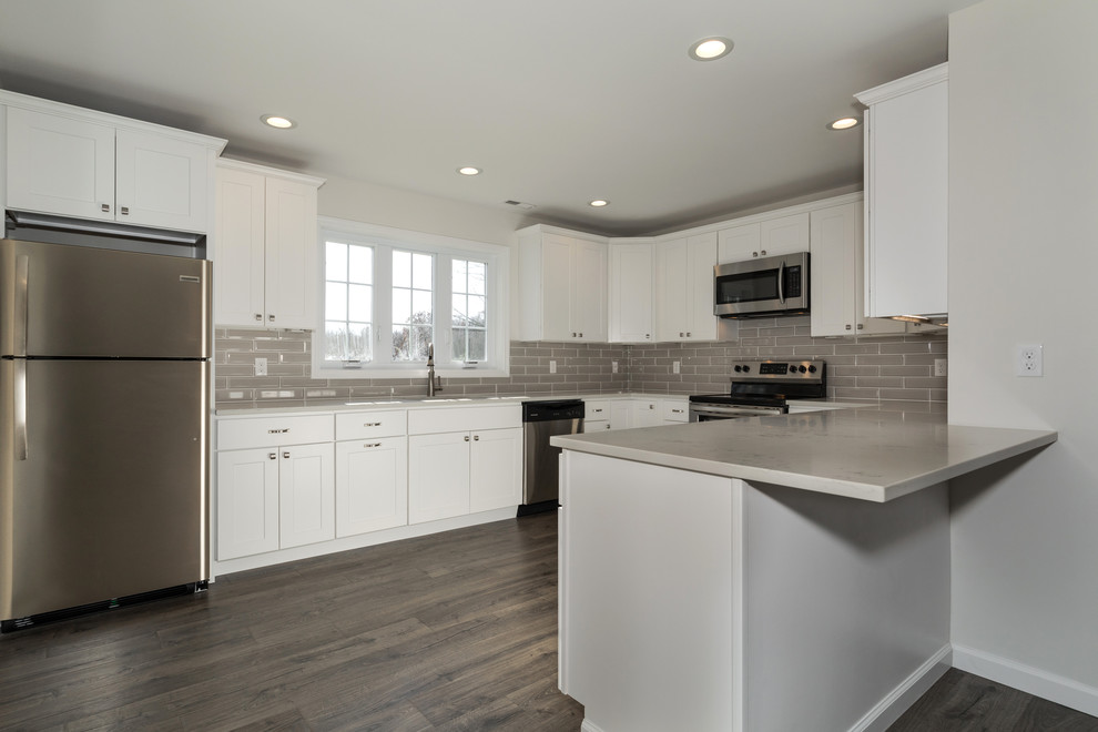 Inspiration for a mid-sized arts and crafts u-shaped eat-in kitchen in New York with an undermount sink, shaker cabinets, white cabinets, quartz benchtops, grey splashback, glass tile splashback, stainless steel appliances, laminate floors, a peninsula and grey floor.