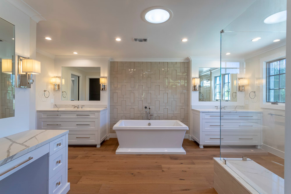 Inspiration for an expansive transitional master bathroom in Los Angeles with white cabinets, a freestanding tub, beige tile, white walls, medium hardwood floors, engineered quartz benchtops, white benchtops and recessed-panel cabinets.