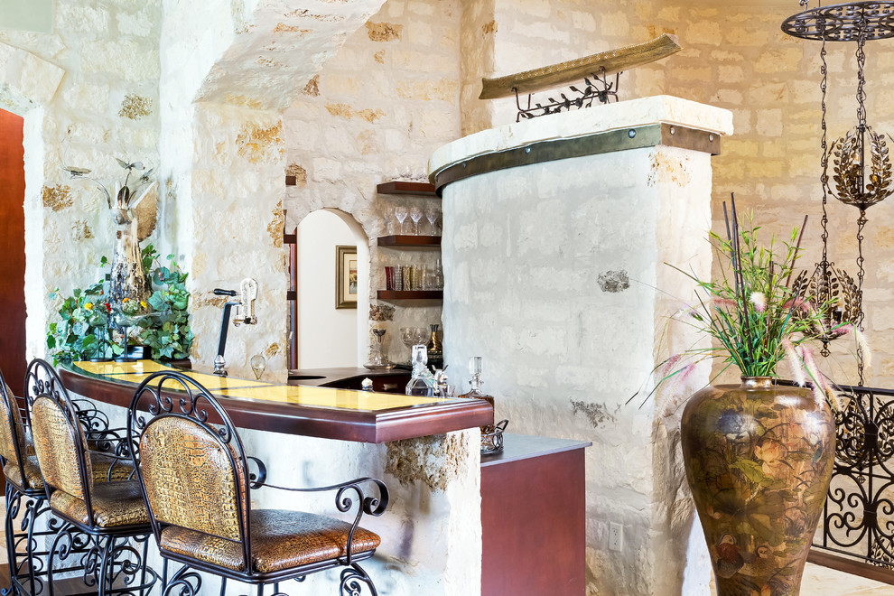 Large mediterranean galley seated home bar in Austin with a drop-in sink, dark wood cabinets, onyx benchtops, beige splashback, stone tile splashback, travertine floors and beige floor.