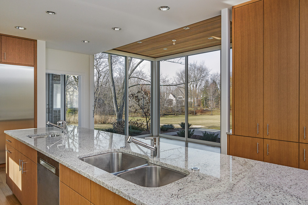 Large modern u-shaped eat-in kitchen in Chicago with a double-bowl sink, flat-panel cabinets, medium wood cabinets, limestone benchtops, grey splashback, limestone splashback, stainless steel appliances, with island, grey benchtop and light hardwood floors.