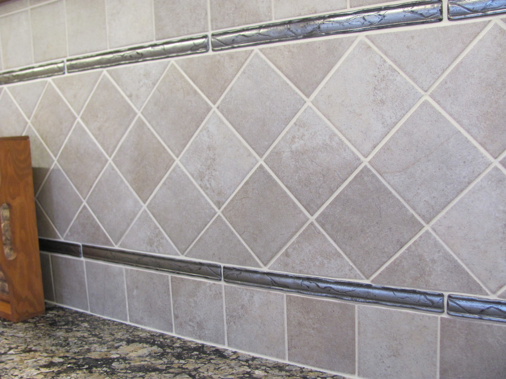 Example of a large classic single-wall home design design with raised-panel cabinets, medium tone wood cabinets, granite countertops, gray backsplash, porcelain backsplash, stainless steel appliances and an island