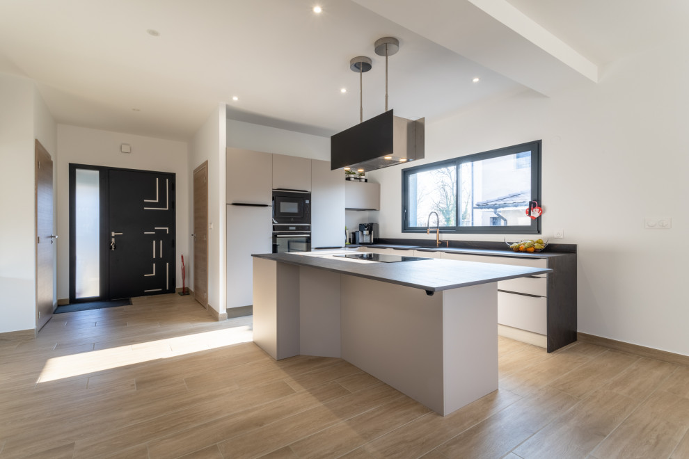 Photo of a medium sized contemporary l-shaped open plan kitchen in Lyon with an integrated sink, beaded cabinets, beige cabinets, tile countertops, black splashback, ceramic splashback, integrated appliances, light hardwood flooring, an island, brown floors and black worktops.