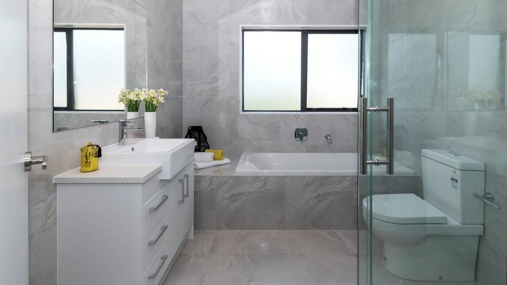 Inspiration for a small transitional bathroom in Auckland with flat-panel cabinets, white cabinets, an alcove tub, a corner shower, a two-piece toilet, gray tile, marble, marble floors, an integrated sink, granite benchtops, grey floor and a hinged shower door.