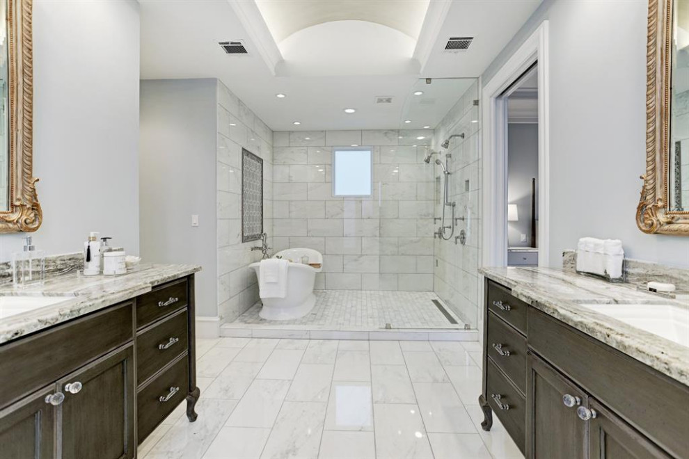 Пример оригинального дизайна: огромная главная ванная комната в стиле неоклассика (современная классика) с фасадами с утопленной филенкой, коричневыми фасадами, отдельно стоящей ванной, душем над ванной, серой плиткой, цементной плиткой, серыми стенами, полом из керамической плитки, врезной раковиной, мраморной столешницей, белым полом, душем с распашными дверями, серой столешницей, тумбой под две раковины, встроенной тумбой и многоуровневым потолком