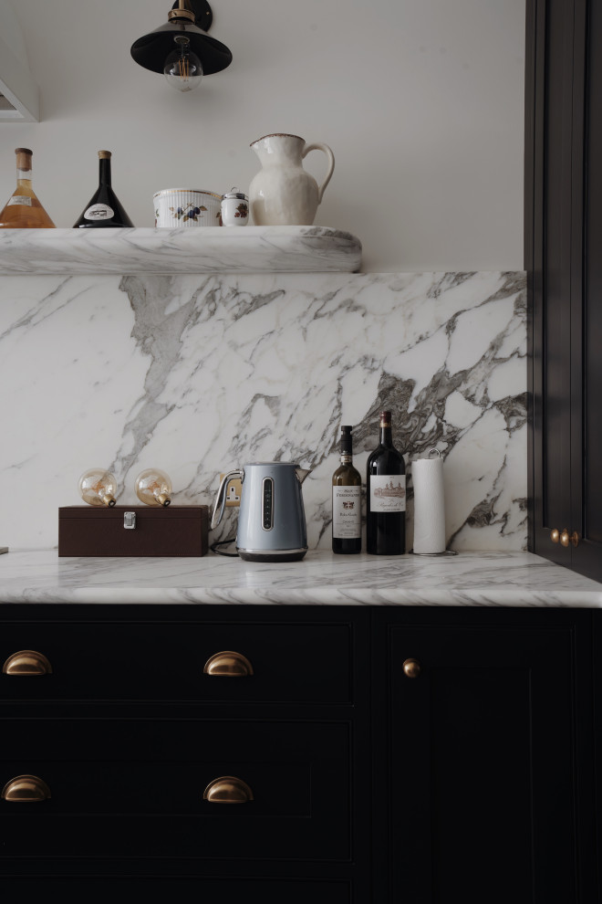 Photo of a medium sized traditional galley kitchen/diner in London with a belfast sink, shaker cabinets, black cabinets, marble worktops, white splashback, marble splashback, black appliances, porcelain flooring, an island, blue floors, white worktops, a vaulted ceiling and feature lighting.