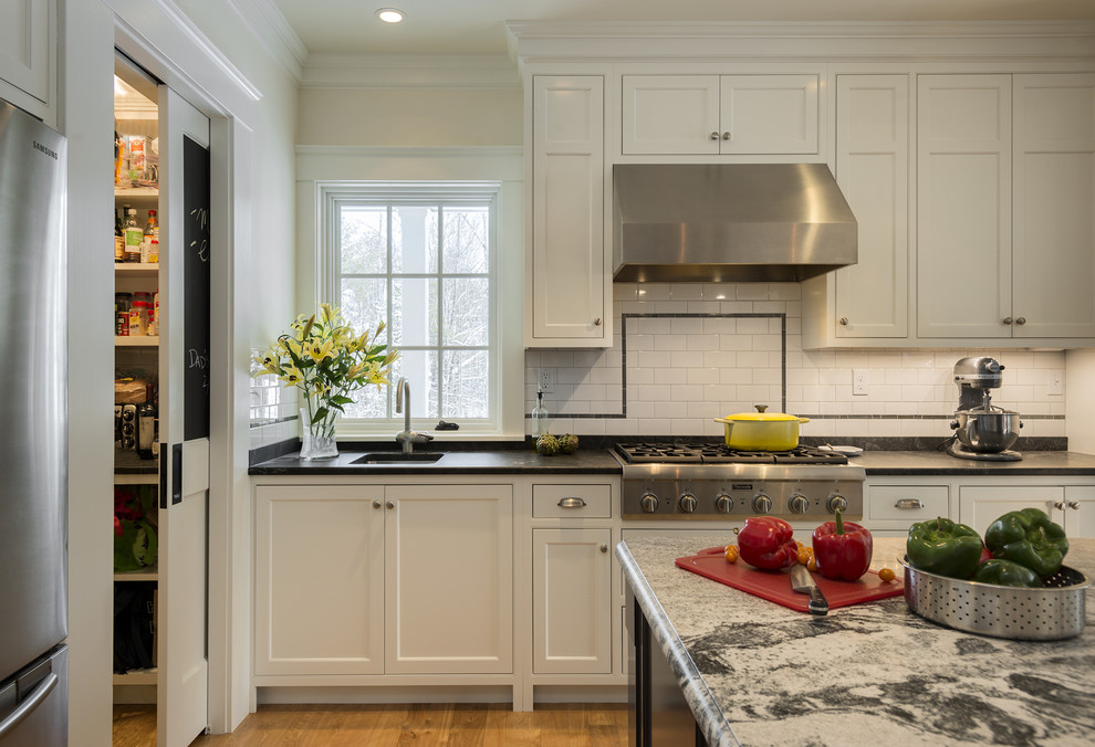Large traditional single-wall eat-in kitchen in Portland Maine with a farmhouse sink, shaker cabinets, white cabinets, granite benchtops, white splashback, ceramic splashback, stainless steel appliances and medium hardwood floors.