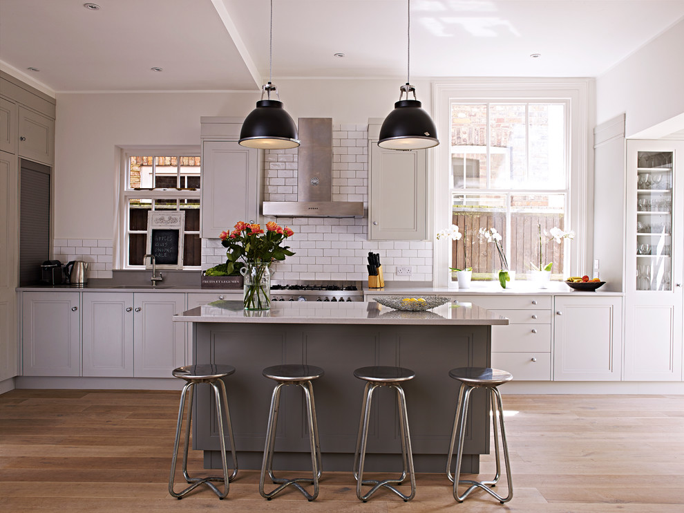 Inspiration for a large transitional eat-in kitchen in London with recessed-panel cabinets, white cabinets, white splashback, subway tile splashback, stainless steel appliances, light hardwood floors and with island.