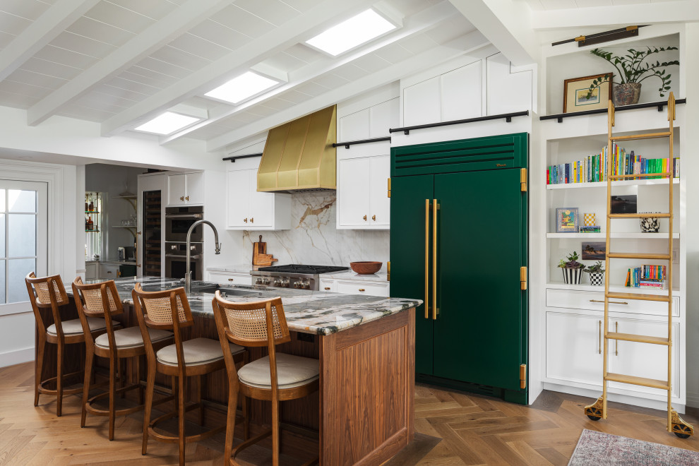 Transitional galley medium tone wood floor, brown floor, exposed beam, shiplap ceiling and vaulted ceiling kitchen photo in Orange County with an undermount sink, flat-panel cabinets, white cabinets, gray backsplash, stone slab backsplash, colored appliances, an island and gray countertops