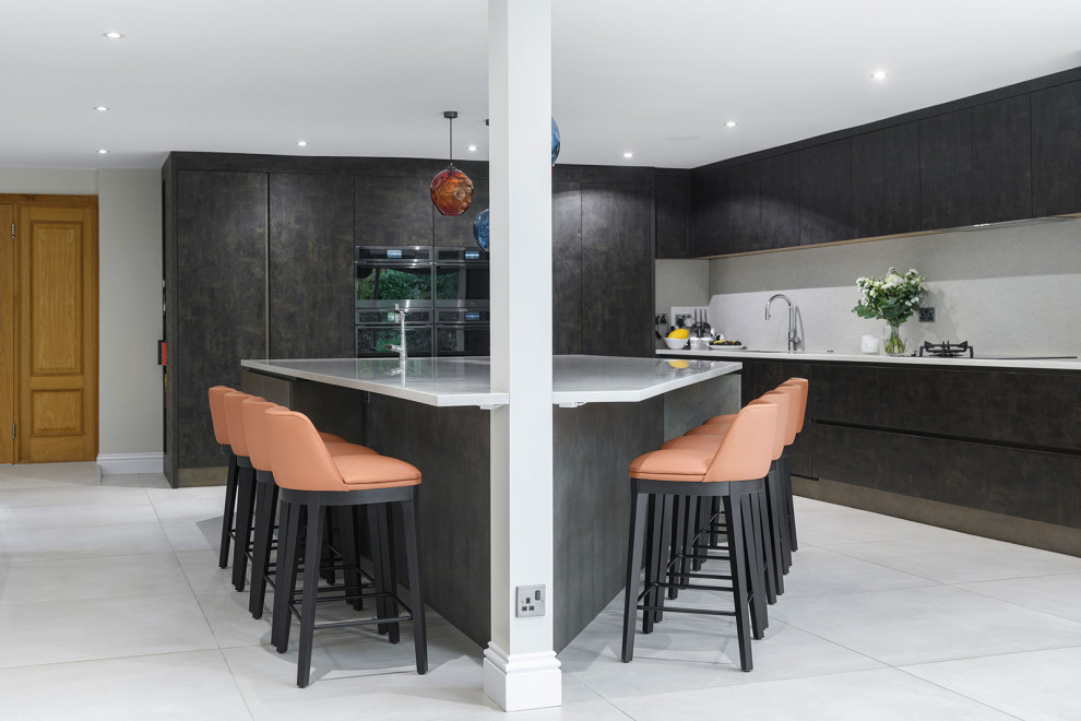 Design ideas for an expansive contemporary open plan kitchen in Berkshire with an integrated sink, flat-panel cabinets, brown cabinets, composite countertops, white splashback, black appliances, porcelain flooring, an island, grey floors, white worktops and feature lighting.