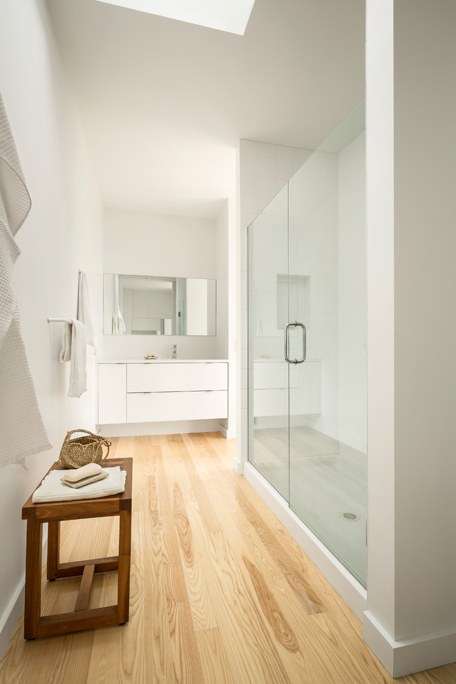 This is an example of a contemporary bathroom in Portland Maine with flat-panel cabinets, white cabinets, an alcove shower and white tile.