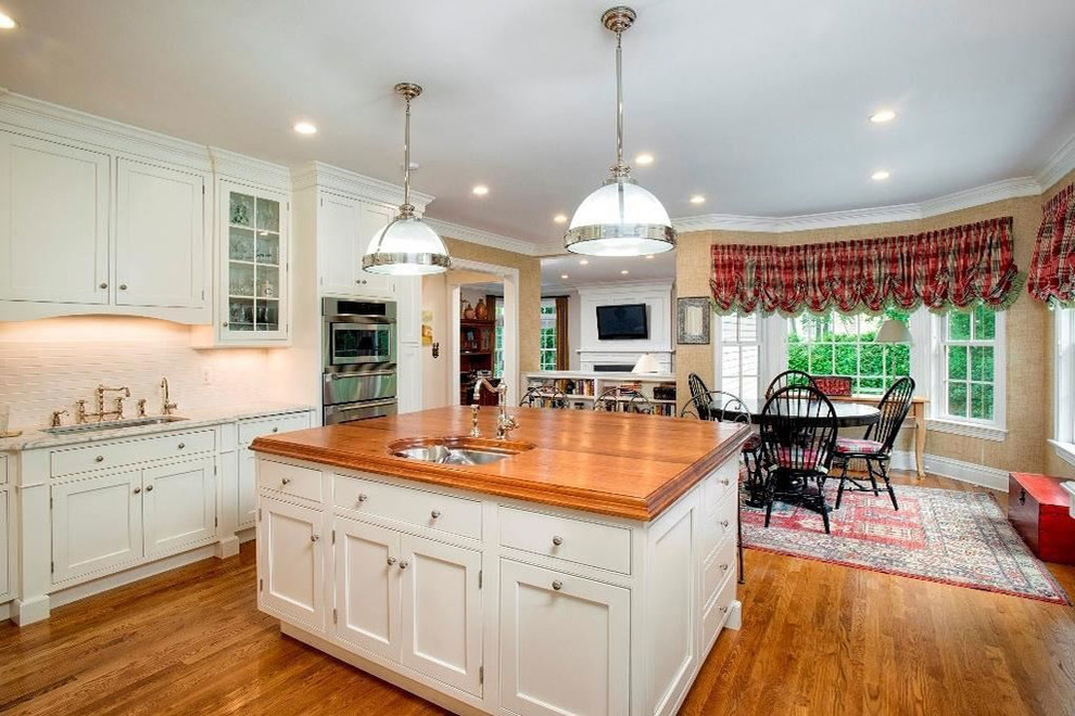 Example of a large classic l-shaped medium tone wood floor and brown floor eat-in kitchen design with an undermount sink, shaker cabinets, white cabinets, white backsplash, stainless steel appliances, an island and wood countertops