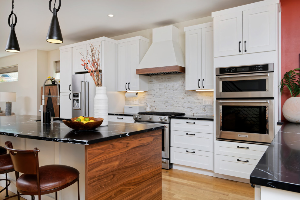 Inspiration for a mid-sized contemporary l-shaped eat-in kitchen in Denver with an undermount sink, shaker cabinets, white cabinets, granite benchtops, white splashback, stainless steel appliances, medium hardwood floors, with island and black benchtop.
