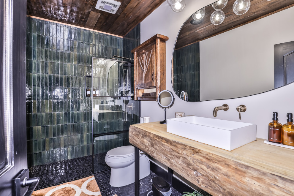 Mid-sized mountain style green tile pebble tile floor, black floor, single-sink and wood ceiling walk-in shower photo with light wood cabinets, a one-piece toilet, a vessel sink, wood countertops, brown countertops and a floating vanity