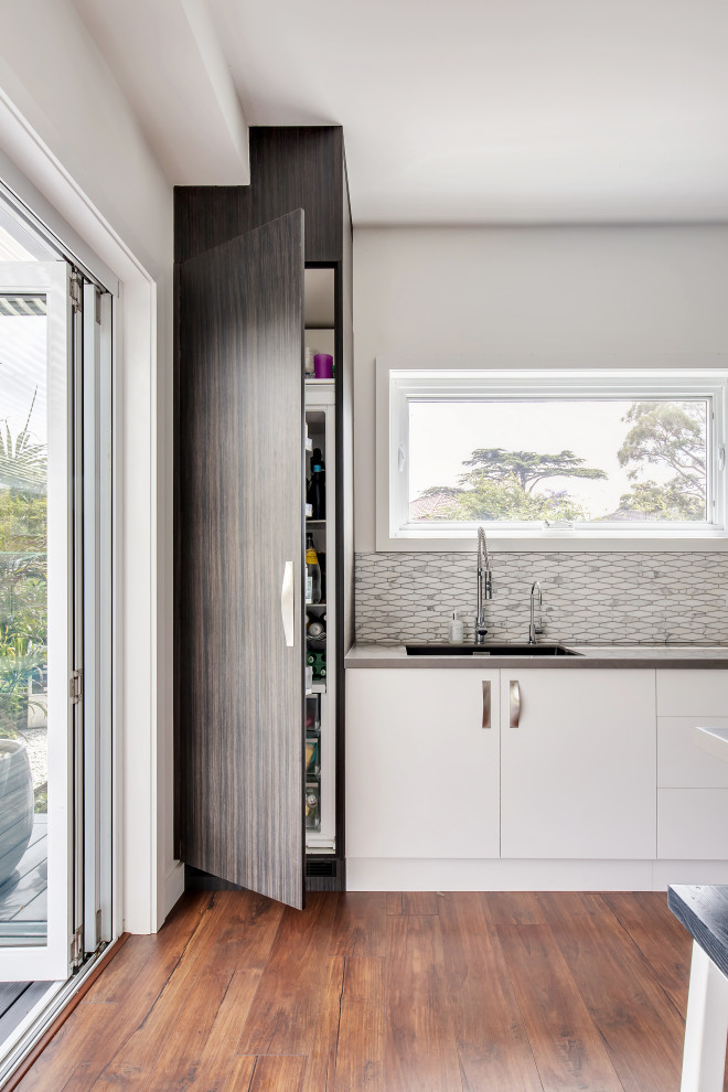 Large contemporary l-shaped kitchen pantry in Sydney with an undermount sink, flat-panel cabinets, dark wood cabinets, solid surface benchtops, multi-coloured splashback, marble splashback, stainless steel appliances, medium hardwood floors, with island, brown floor and grey benchtop.