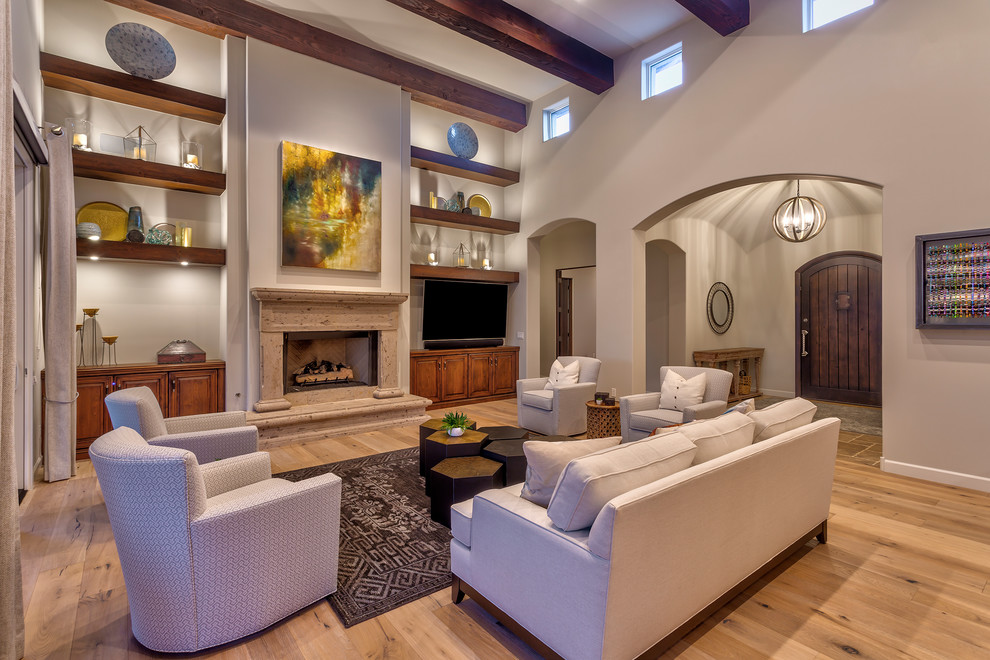 Inspiration for an expansive open concept living room in Phoenix with grey walls, light hardwood floors, a standard fireplace, a plaster fireplace surround, a wall-mounted tv and brown floor.