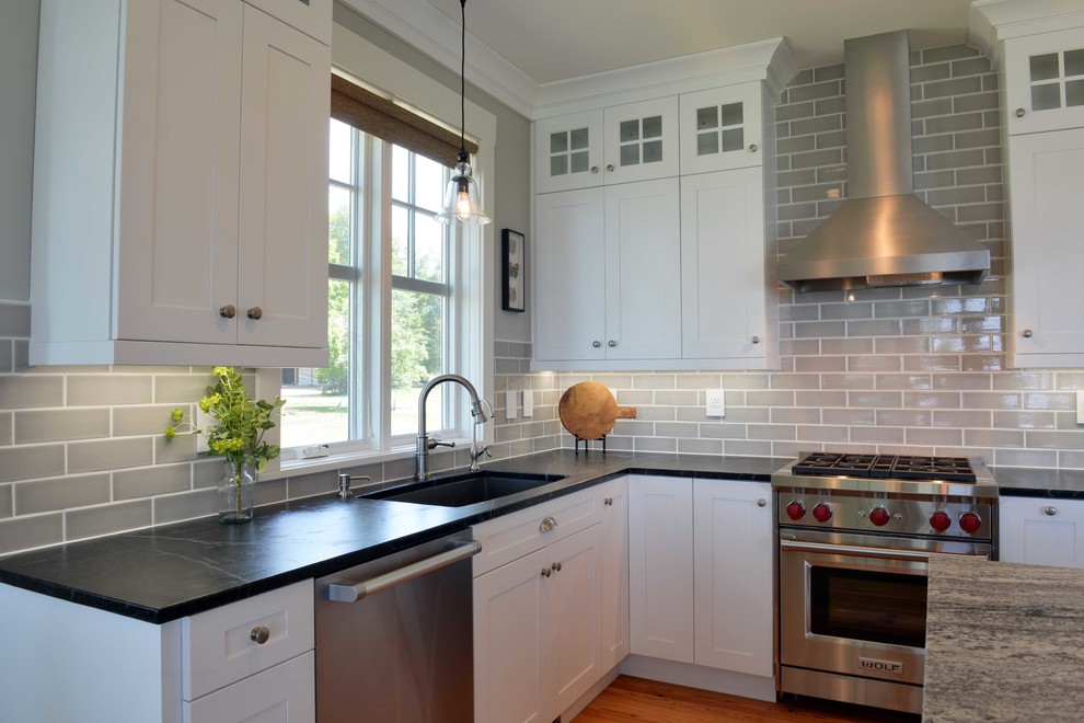 Example of a mid-sized transitional l-shaped light wood floor and beige floor eat-in kitchen design with shaker cabinets, white cabinets, granite countertops, gray backsplash, subway tile backsplash, stainless steel appliances, an island and an undermount sink
