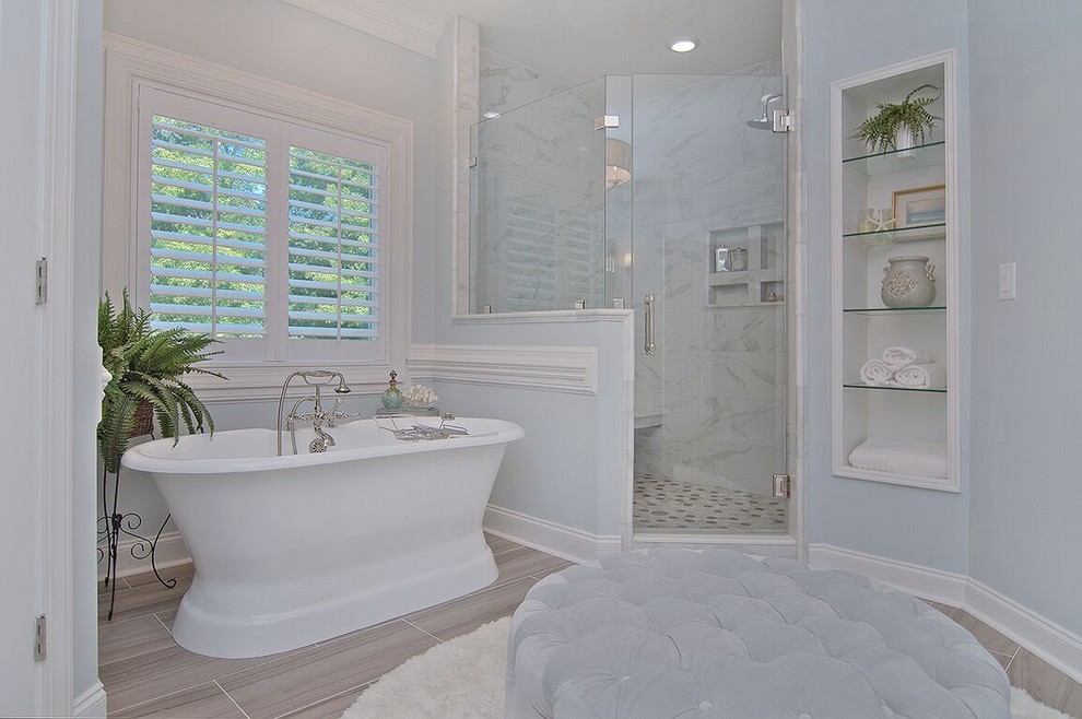 Photo of a large transitional master bathroom in Charlotte with a freestanding tub, an alcove shower, gray tile, marble, blue walls, vinyl floors, marble benchtops, brown floor, a hinged shower door, shaker cabinets, white cabinets, a two-piece toilet and an undermount sink.