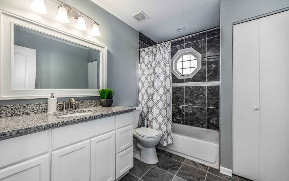This is an example of a mid-sized transitional master bathroom in Chicago with recessed-panel cabinets, white cabinets, an alcove tub, a shower/bathtub combo, a one-piece toilet, grey walls, an undermount sink, terrazzo benchtops, black floor and a shower curtain.