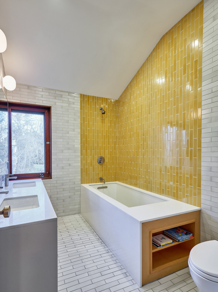 This is an example of a mid-sized midcentury kids bathroom in New York with flat-panel cabinets, grey cabinets, an undermount tub, a two-piece toilet, multi-coloured tile, ceramic tile, multi-coloured walls, ceramic floors, an undermount sink, engineered quartz benchtops, white floor and grey benchtops.