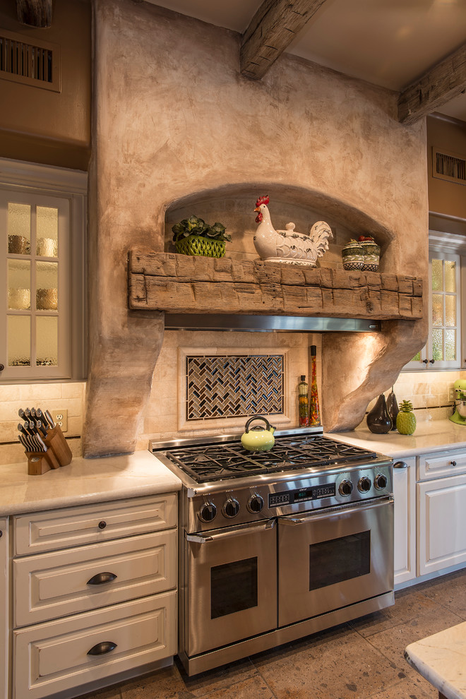 Photo of a large country l-shaped open plan kitchen in Phoenix with a farmhouse sink, raised-panel cabinets, white cabinets, granite benchtops, beige splashback, stone tile splashback, stainless steel appliances, travertine floors and with island.