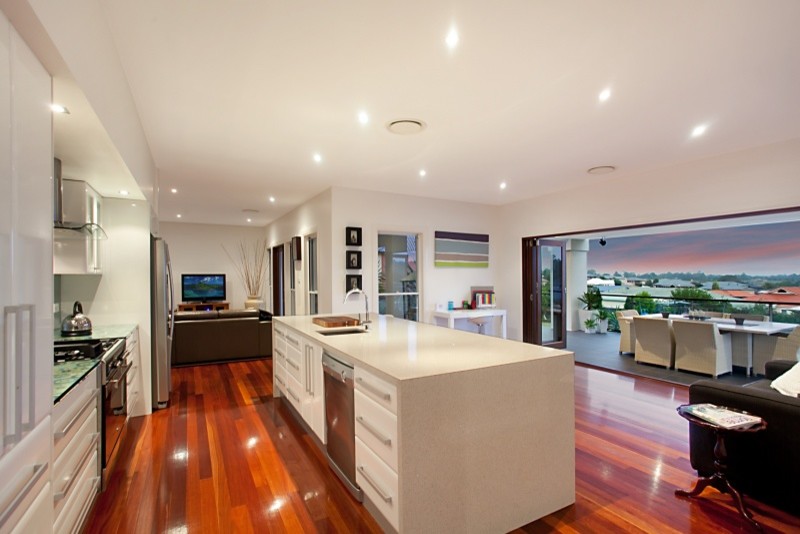 Design ideas for a mid-sized contemporary single-wall open plan kitchen in Newcastle - Maitland with a single-bowl sink, flat-panel cabinets, white cabinets, granite benchtops, green splashback, glass sheet splashback, stainless steel appliances, medium hardwood floors and with island.