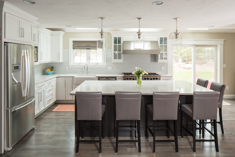 Inspiration for a large transitional l-shaped eat-in kitchen in Boston with a farmhouse sink, recessed-panel cabinets, white cabinets, stainless steel appliances, with island, quartz benchtops, green splashback, glass tile splashback, porcelain floors and brown floor.