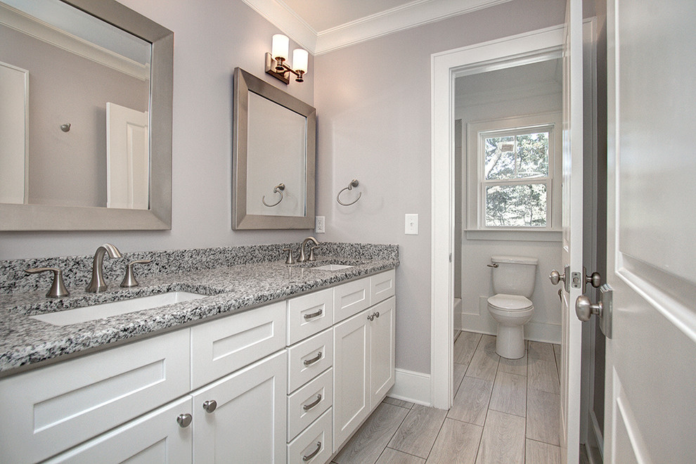 Photo of a mid-sized transitional kids bathroom in Charlotte with shaker cabinets, white cabinets, a drop-in tub, a shower/bathtub combo, a two-piece toilet, gray tile, porcelain tile, grey walls, ceramic floors, an undermount sink and granite benchtops.