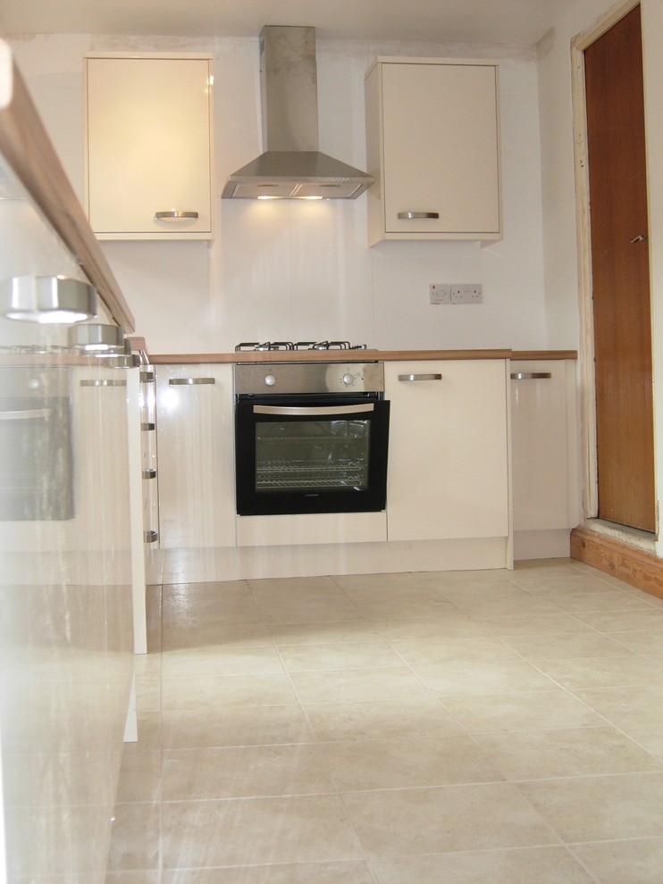 Mid-sized contemporary l-shaped separate kitchen in London with a single-bowl sink, flat-panel cabinets, black cabinets, laminate benchtops, beige splashback, ceramic splashback, stainless steel appliances, ceramic floors and no island.