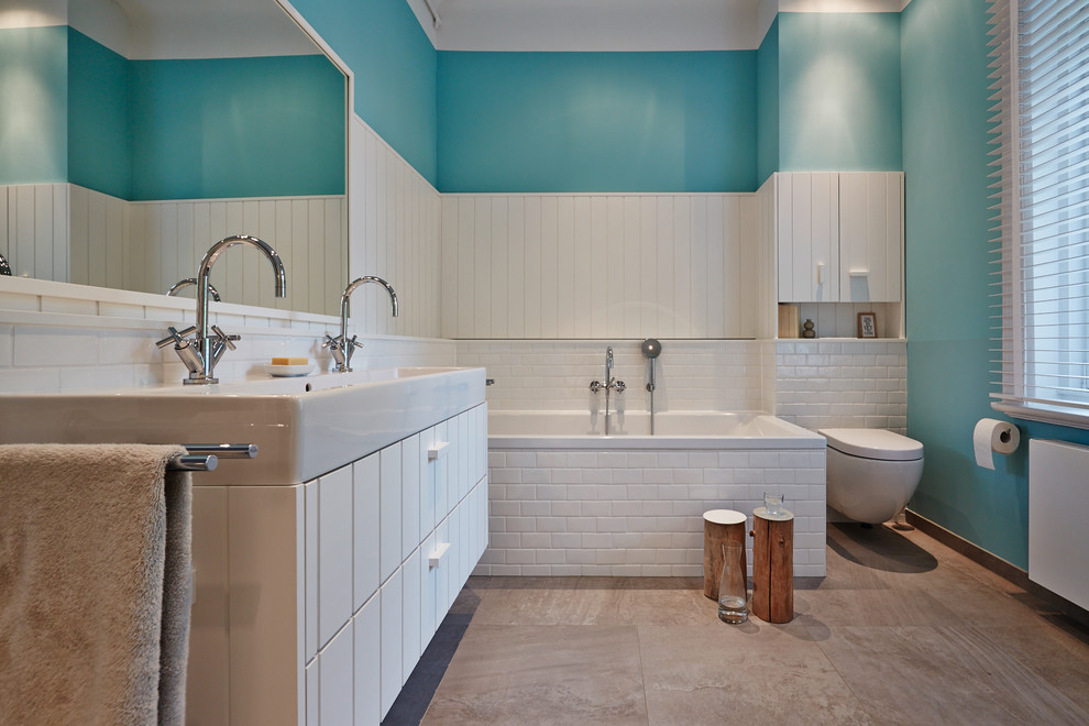 Photo of a large contemporary bathroom in Hamburg with a trough sink, white cabinets, a drop-in tub, a wall-mount toilet, white tile, subway tile, blue walls, flat-panel cabinets and a shower/bathtub combo.