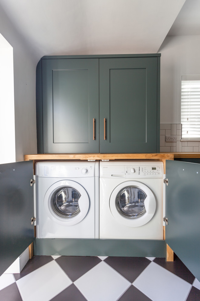 Inspiration for a mid-sized transitional galley laundry room in Manchester with a farmhouse sink, shaker cabinets, green cabinets, wood benchtops, white splashback, subway tile splashback, porcelain floors, white floor and brown benchtop.