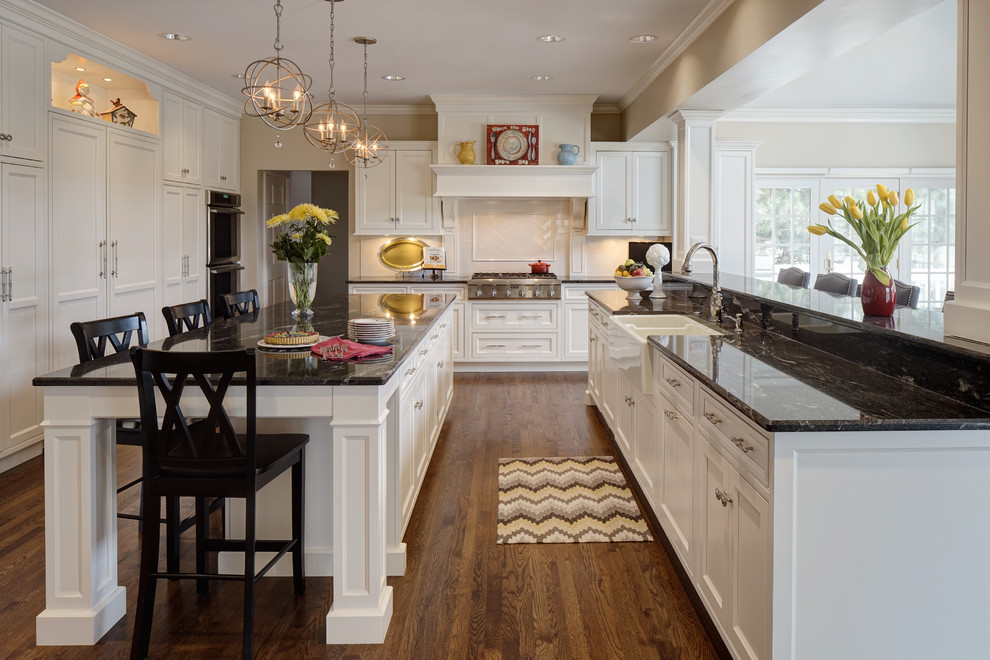 Photo of a large traditional u-shaped open plan kitchen in Chicago with a farmhouse sink, beaded inset cabinets, white cabinets, granite benchtops, white splashback, ceramic splashback, panelled appliances, medium hardwood floors and with island.