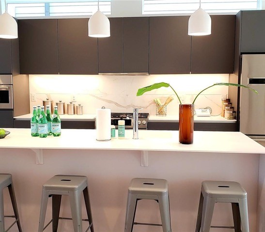 Inspiration for a mid-sized modern galley open concept kitchen remodel in Denver with an undermount sink, flat-panel cabinets, dark wood cabinets, quartz countertops, white backsplash, porcelain backsplash, stainless steel appliances, an island and white countertops