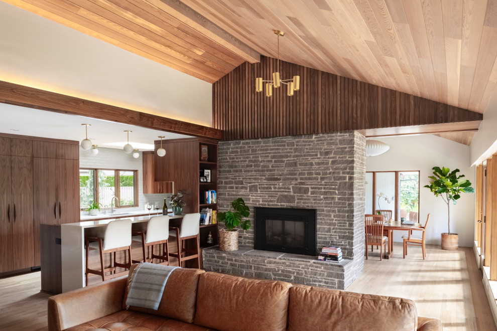 Photo of a midcentury open concept living room in Portland with white walls, light hardwood floors, a standard fireplace, vaulted and wood.